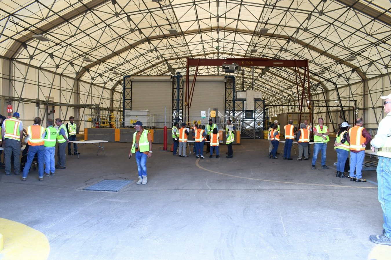 Lots of people inside a large building, they wear orange and yellow safety vests
