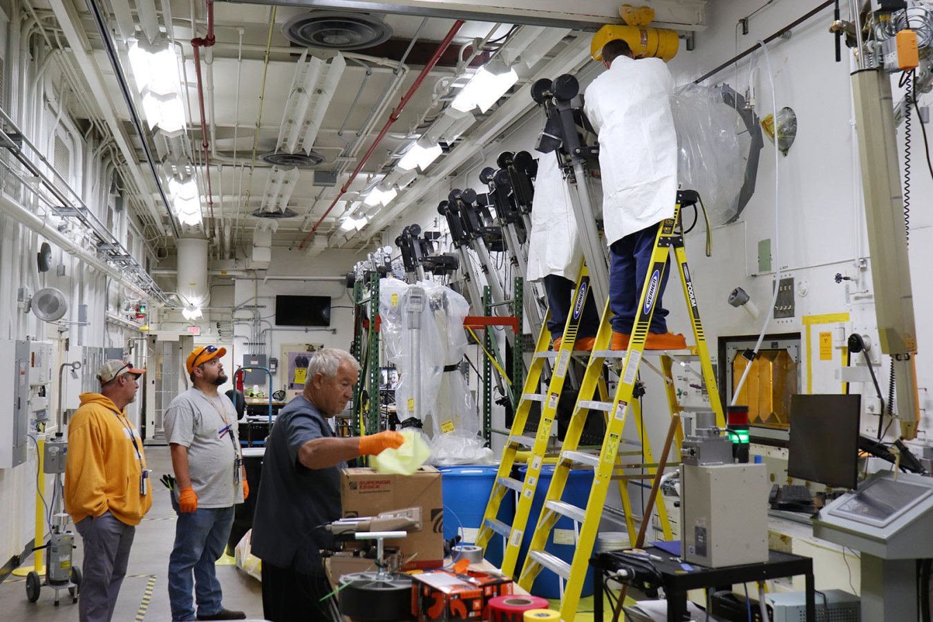 Workers stand on ladders, while others stand on the ground and work to install a hot cell 