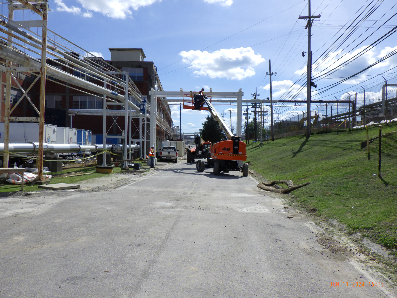 A construction site with a building with lots of metal pipes and a construction vehicle drives on the road