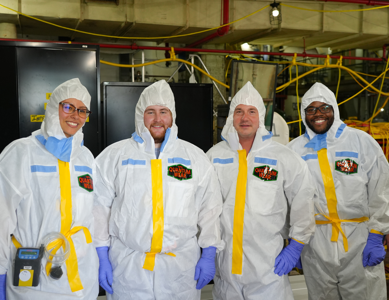 Four student interns in white hazmat suits stand in a laboratory 