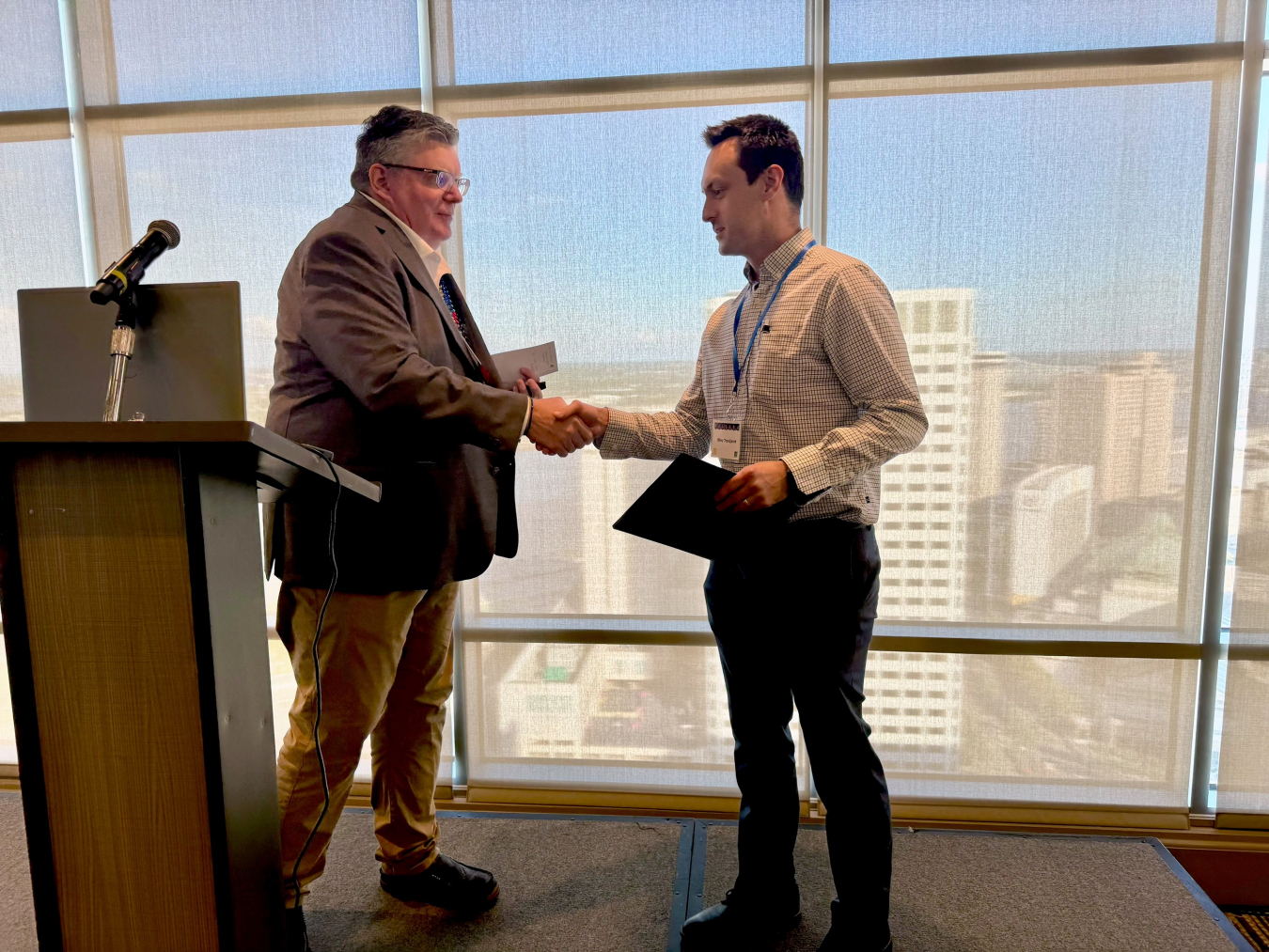 Two men stand beside a podium and shake hands