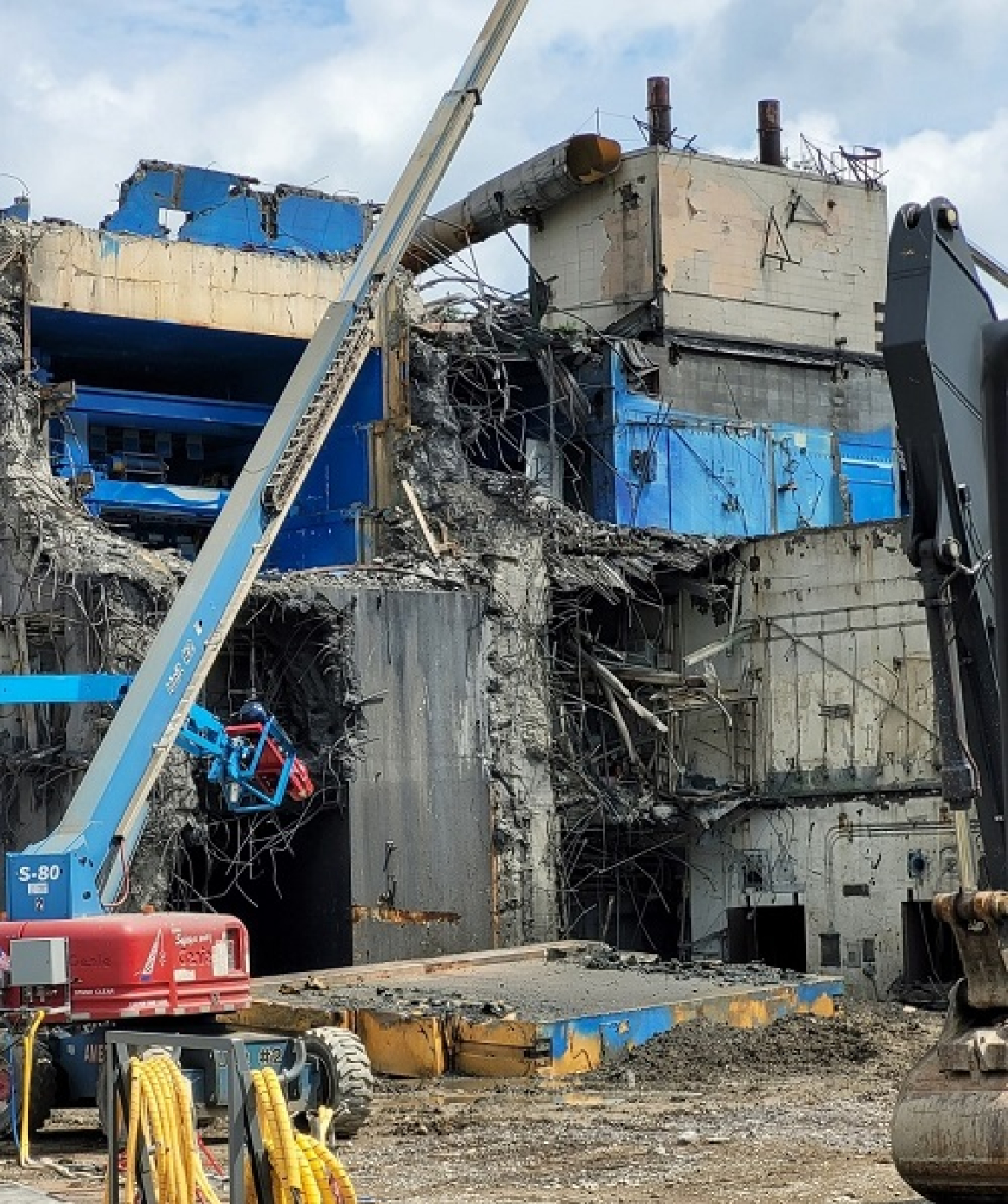A crane works on demolishing a building, a large door from the building can be seen on the ground beside the crane