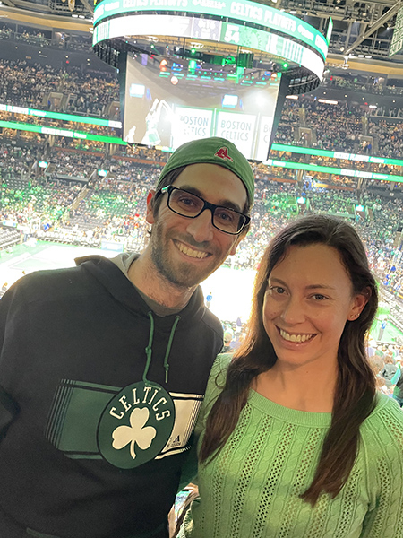 A couple posing inside an indoor stadium wearing green with Celtics logos