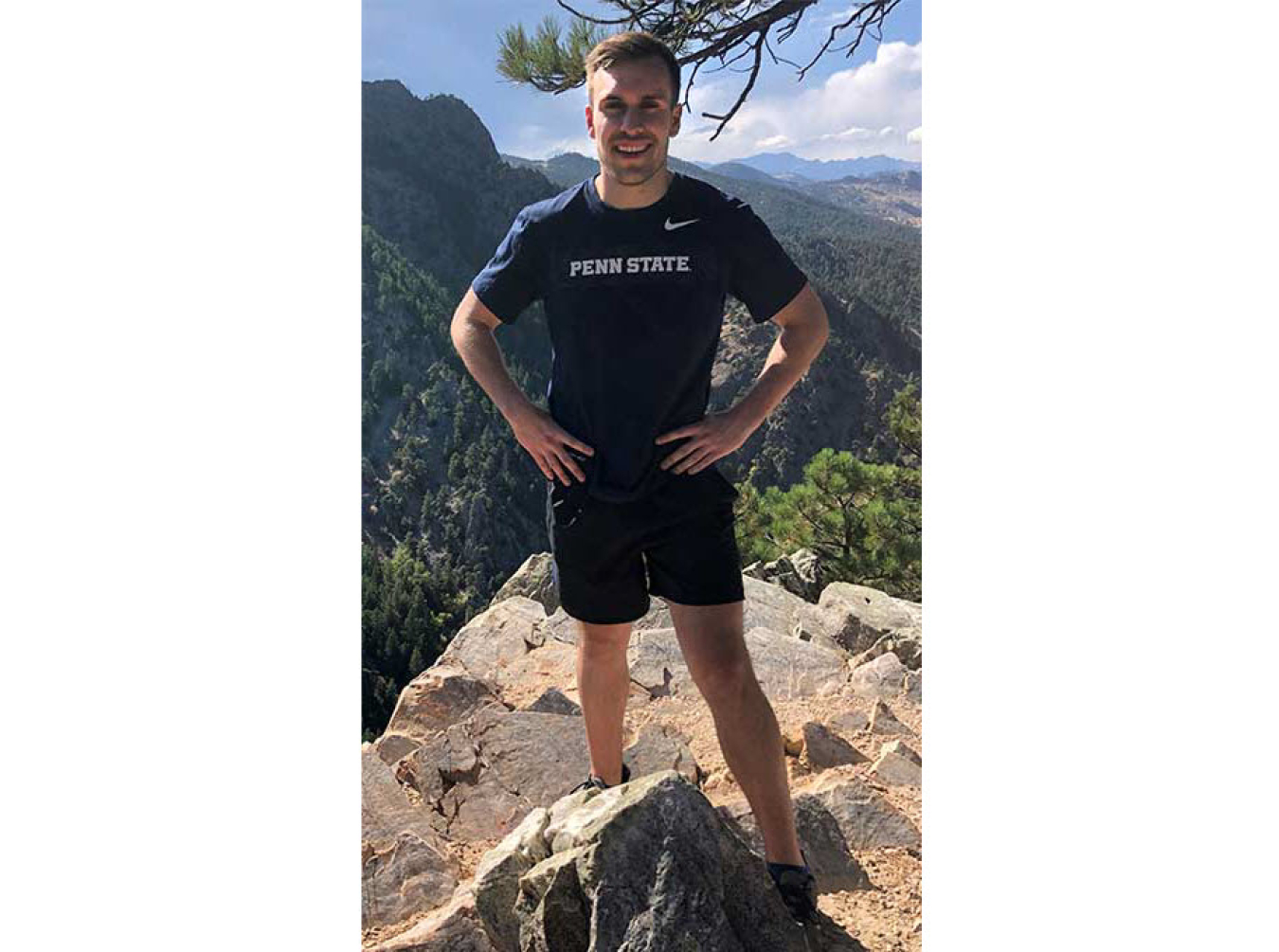 Gage Reber standing on rocky ground with green mountains in background.
