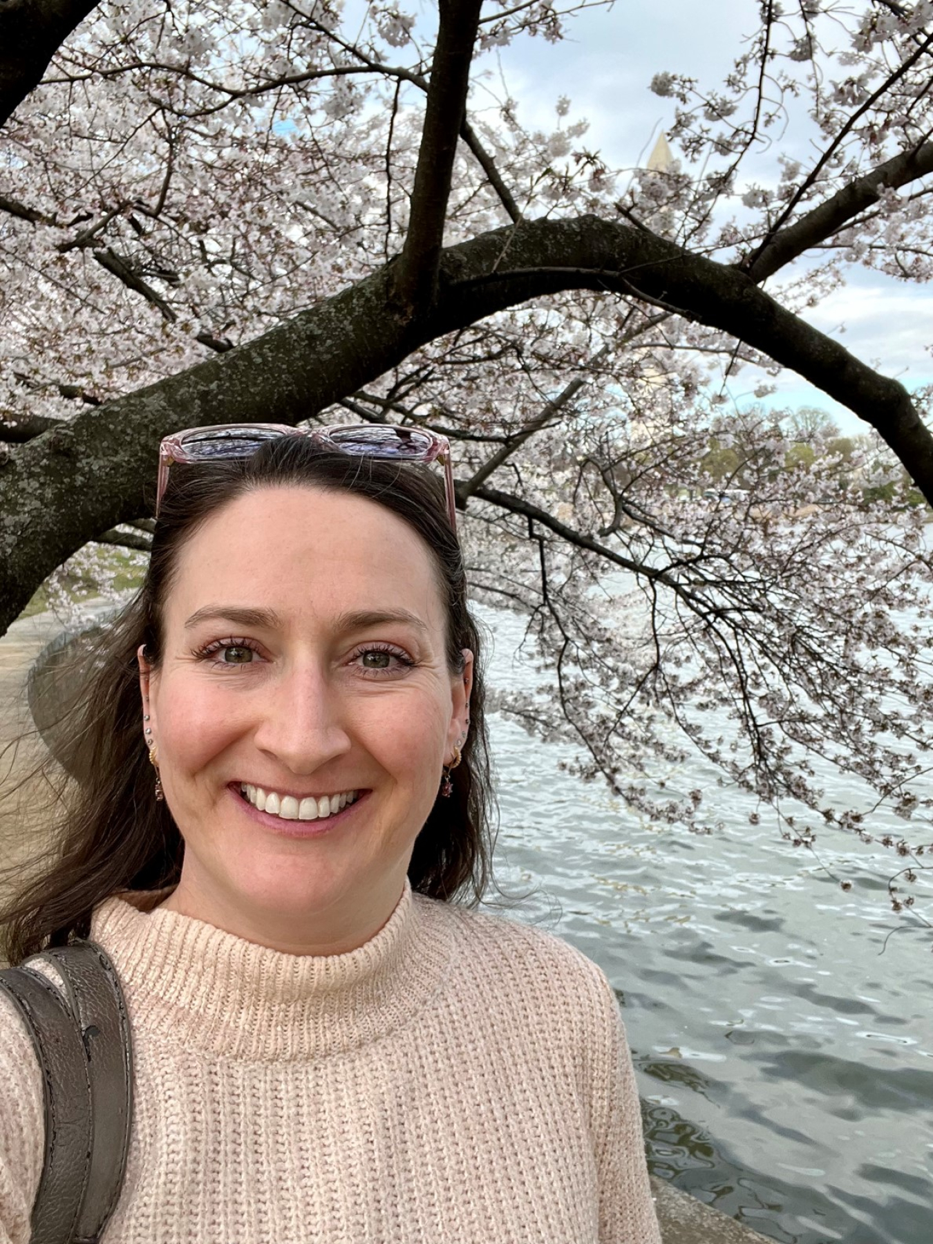 A woman near a body of water and overhanging trees smiles for the camera. 