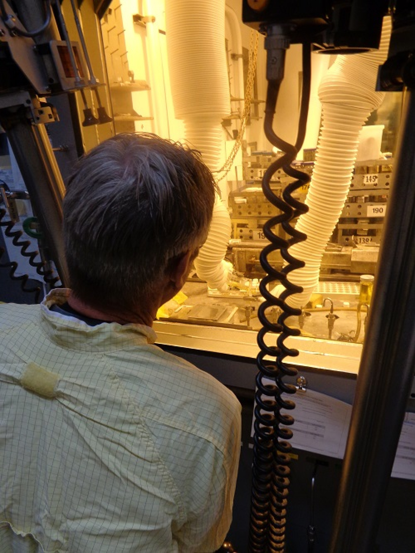 A man stands with his back towards the camera and looks inside a glass container with yellow lights and tubes inside of it