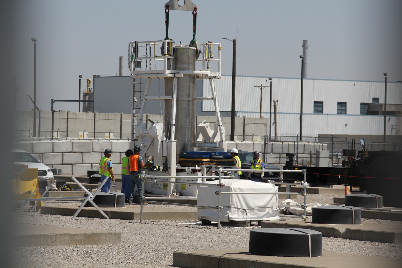 Workers stand beside a large white machine with a metal pipe sticking out of it