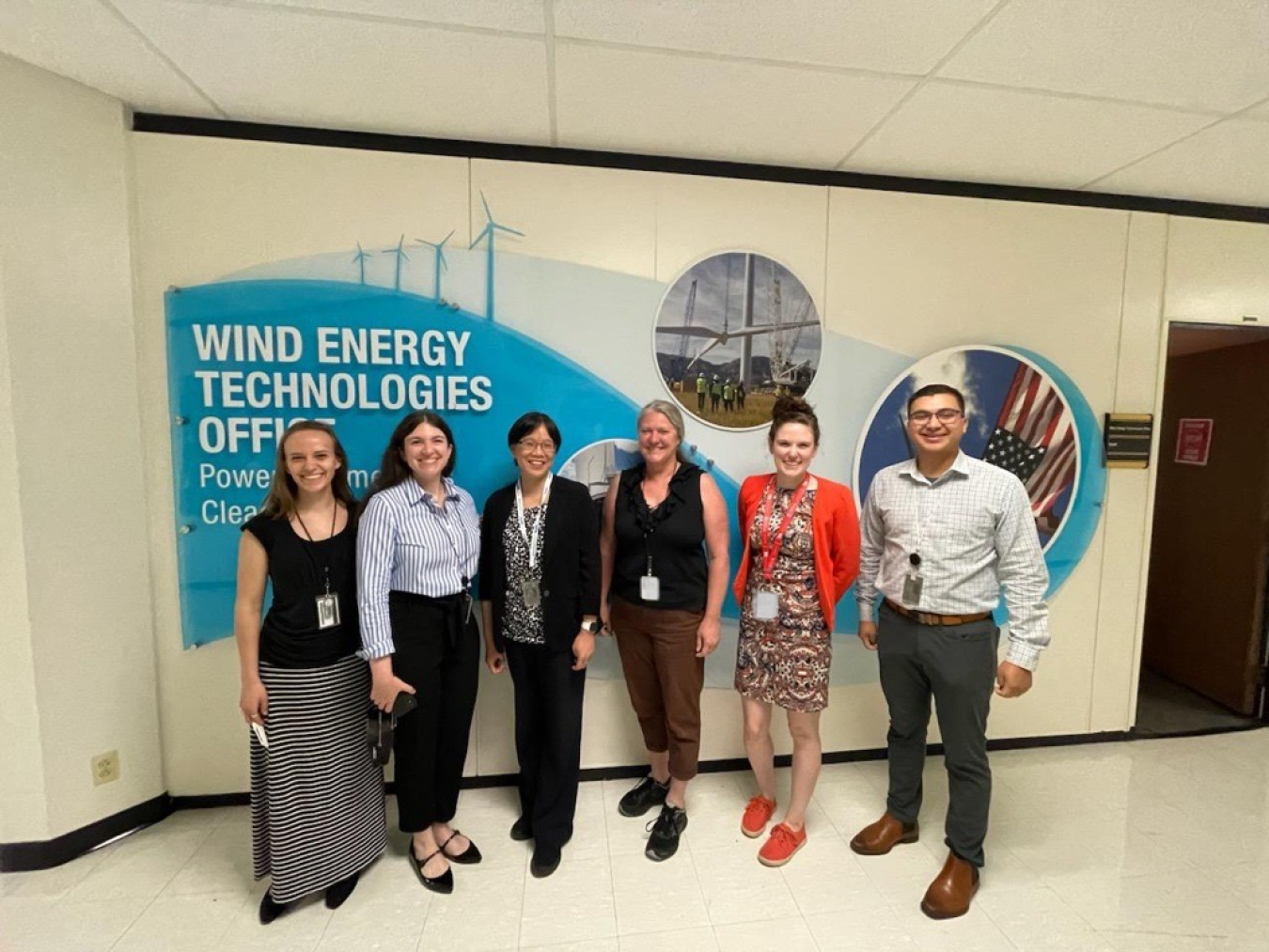 Six people dressed in business casual clothes standing in front of the Wind Energy Technologies Office sign