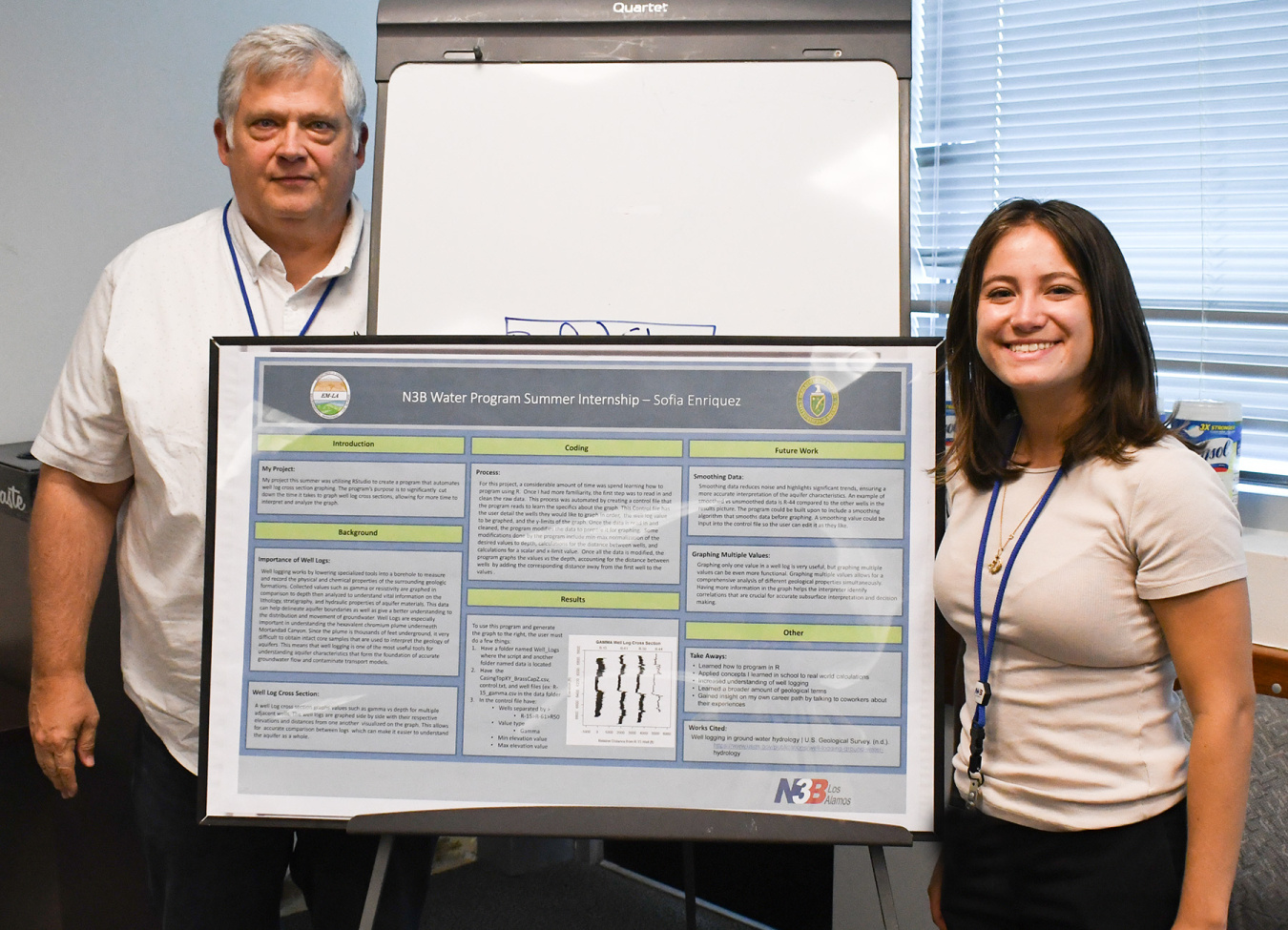 Two individuals stand beside a poster board and smile