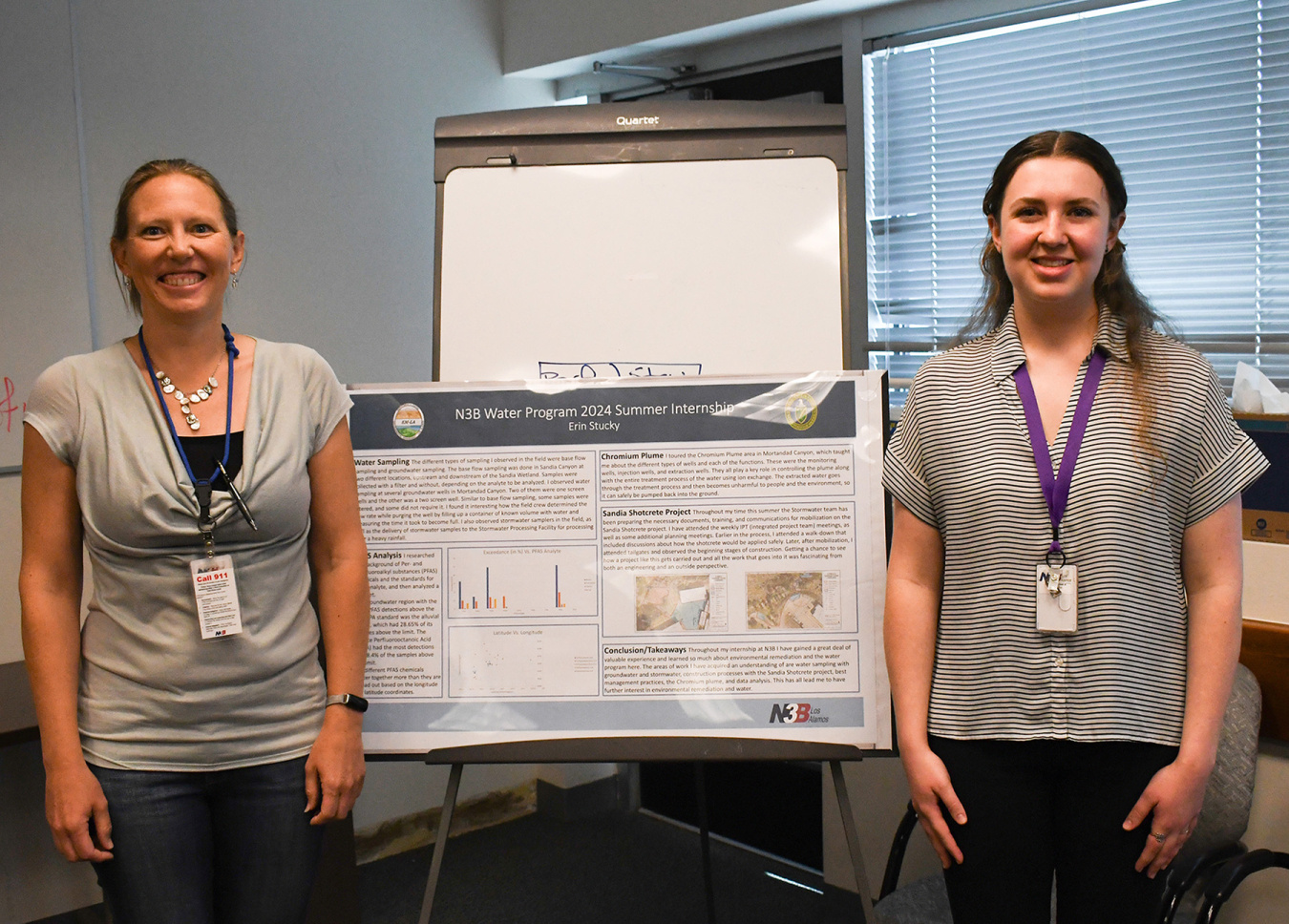 Two individuals stand beside a poster board and smile