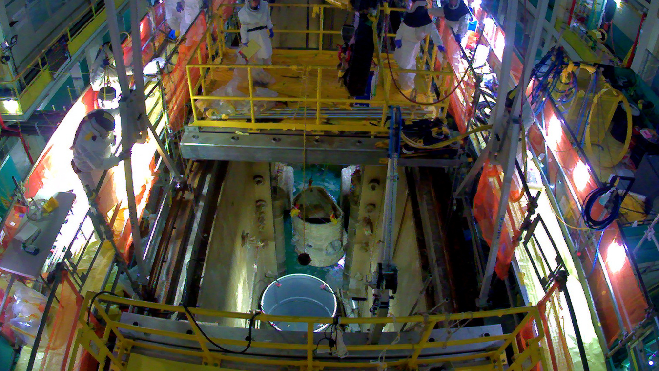 An overhead view of the inside of a facility building with lots of pipes and tubes. Workers stand inside and carry out their jobs