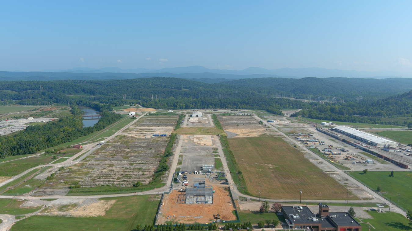 An aerial view of a large plot of land with multiple different sized building, open lots of dirt, trees, and grass