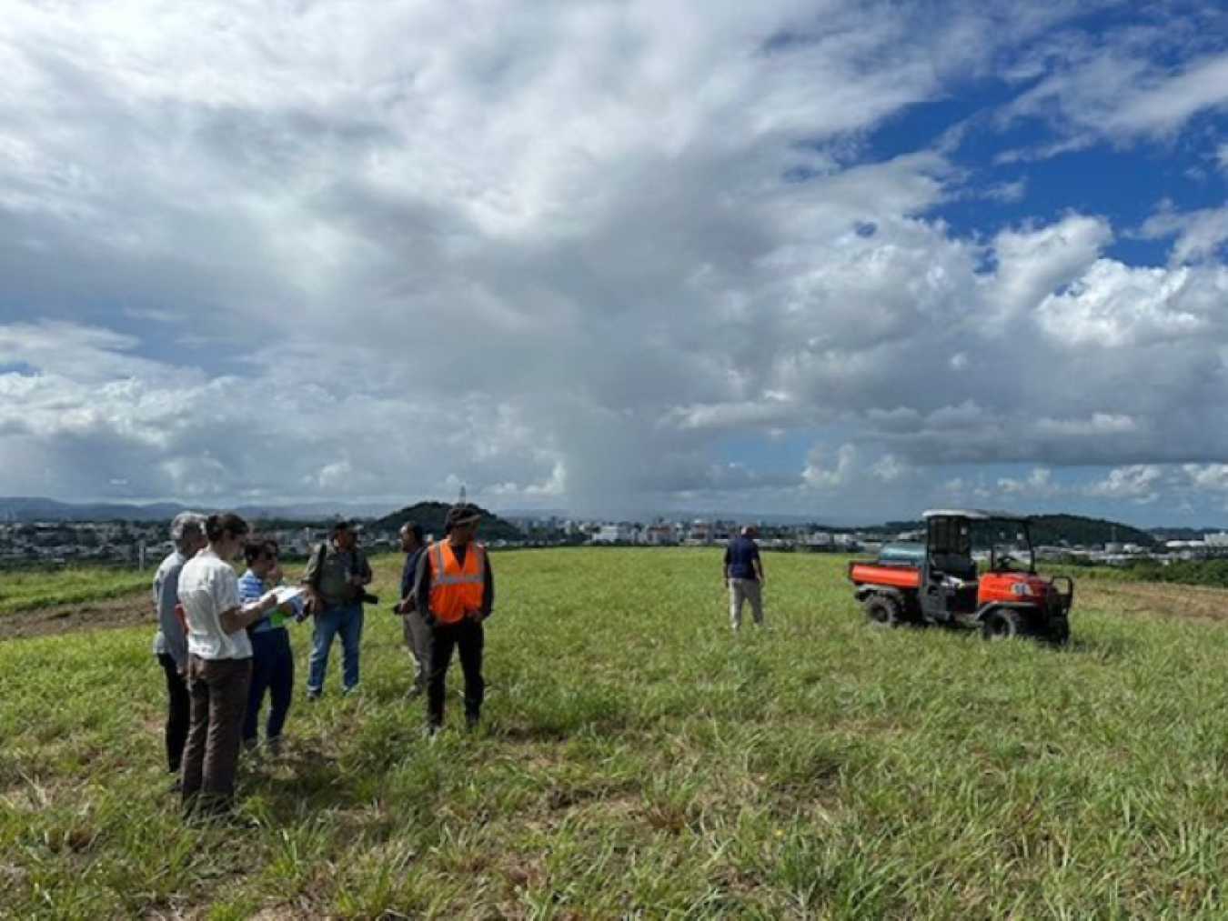 People standing in a field with an all-terrain vehicle parked in the distance