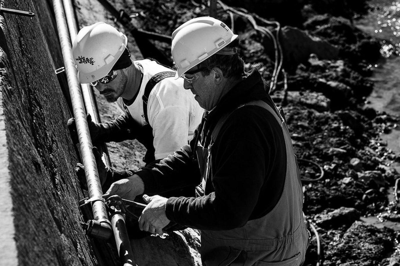 Two men in hard hats work together to attach a pipe.