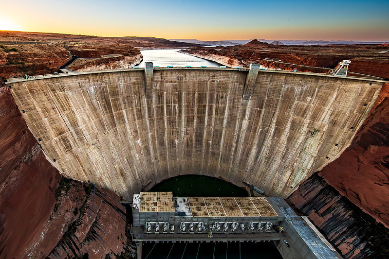 Sunset view of the enormous Glen Canyon Dam in Arizona, with rocky plateaus on both sides of the Colorado River.