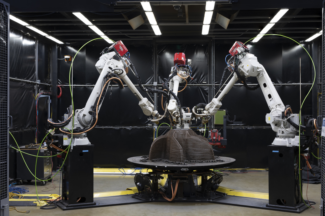 Large mechanical arms construct a metal object.