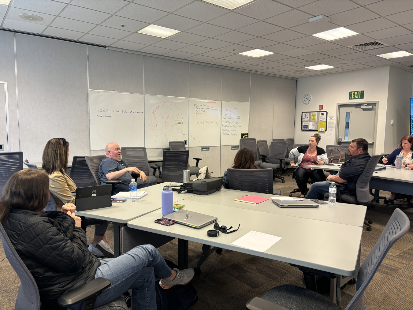 A group of individuals inside a classroom sitting at tables and talking to each other