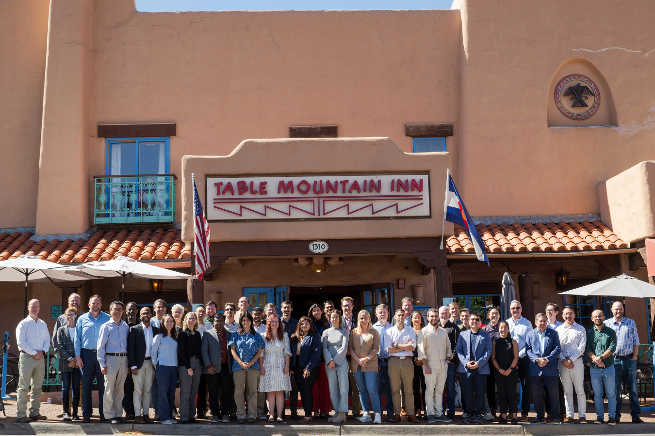 A group of 50 people stand outside in front of a building, smiling for the camera. 