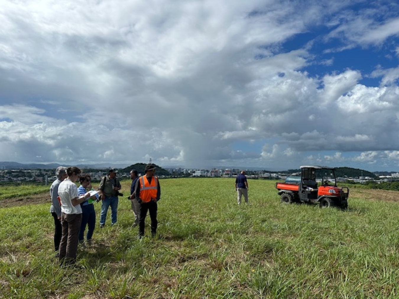 NREL researchers visiting a brownfield site in Puerto Rico. A cloud-filled blue sky appears in the background.