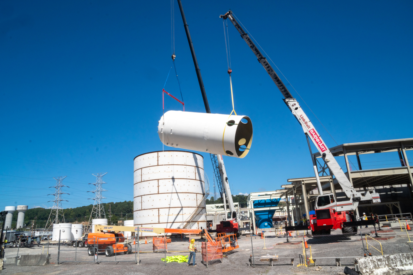 Cranes and work utility vehicles lift part of a large tank onto the base of it