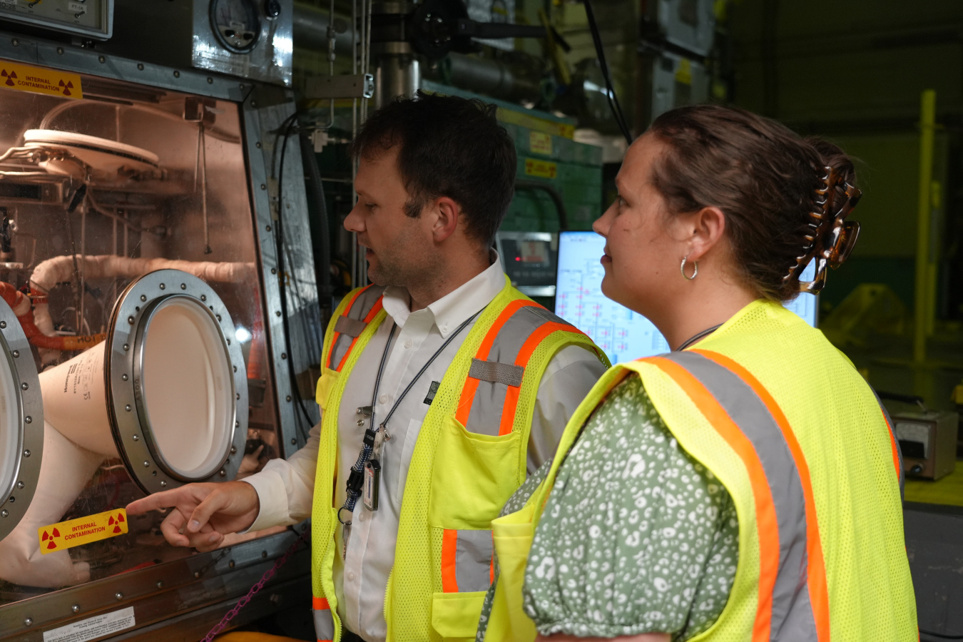 Two employees in yellow safety vest look at a machine