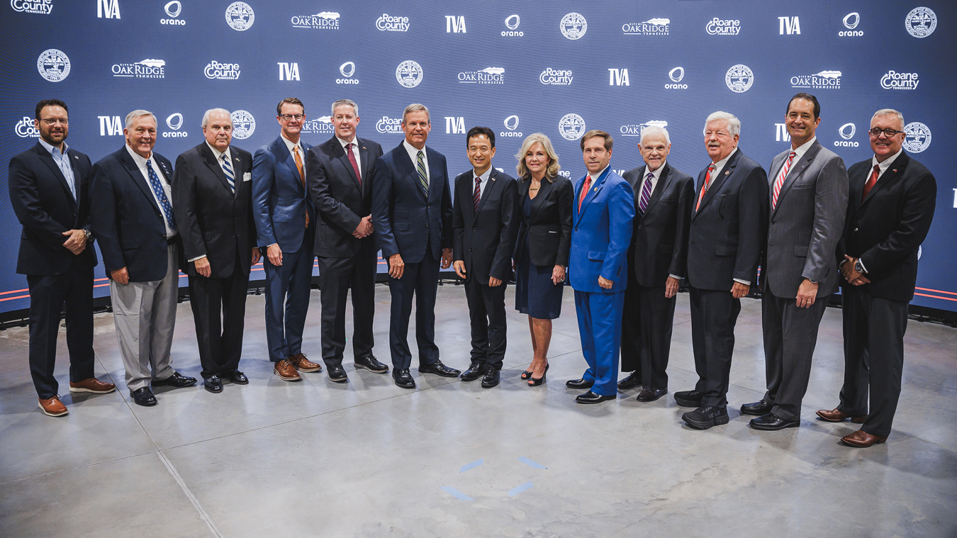 A group of people in suits stand in front of a dark blue backdrop and pose for a group picture