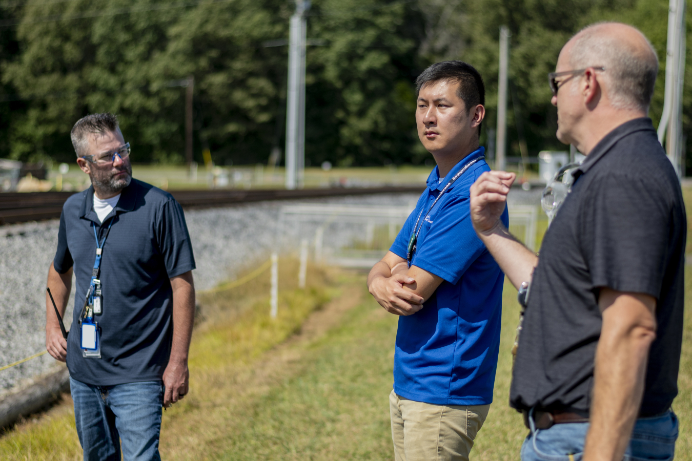 3 men stand outside in a work site and speak to each other