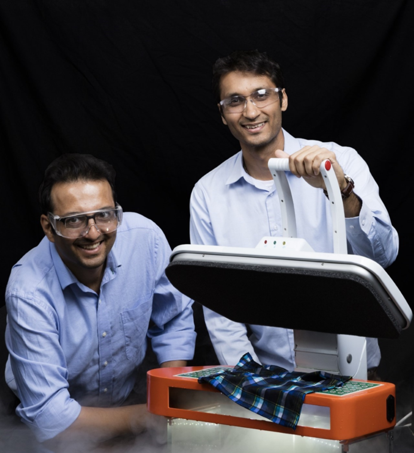 Two men smile for the camera behind a piece of mechanical equipment with fabric on it.