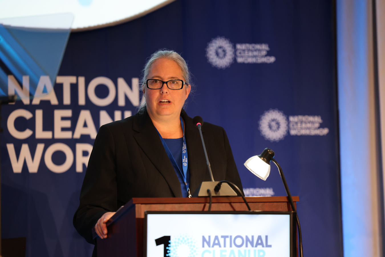A woman standing on a stage speaking at a podium while looking out into the audience
