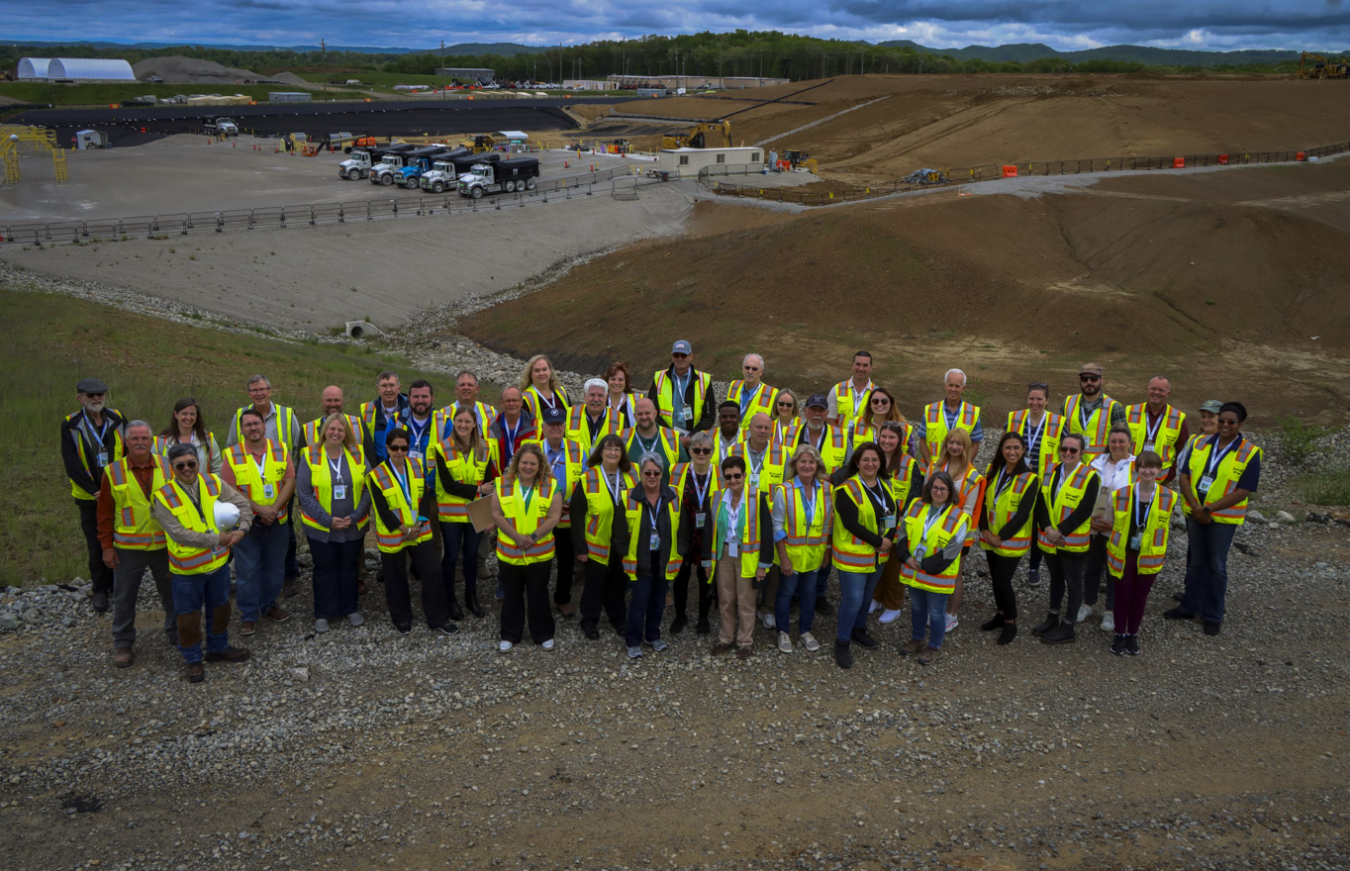 A large group of people in yellow safety vests pose at a work site for a group picture