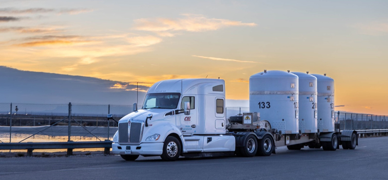 Photo of a large hauling vehicle with three large containers loaded on the bed.