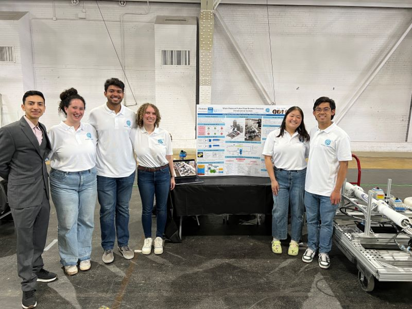 A photo containing six people posing with a poster and equipment.