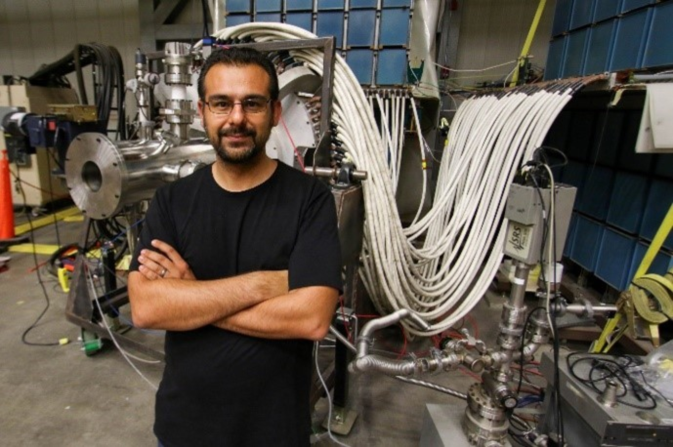 Worker at a national laboratory standing with arms crossed in front of machinery.
