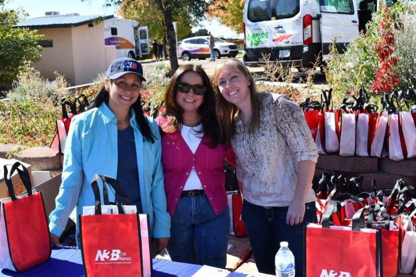 Three women stand at a booth outside and smile for a group picture