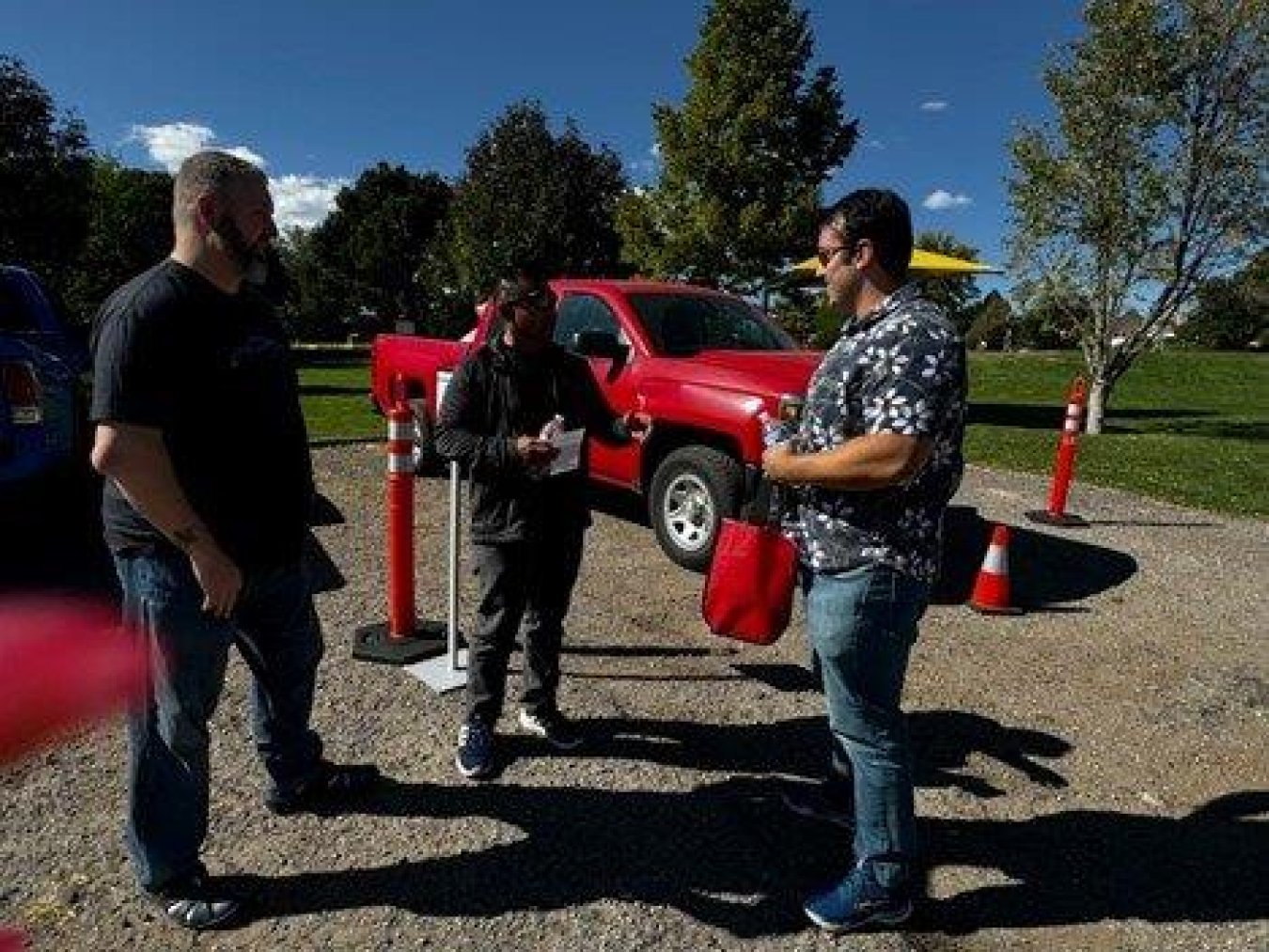 Three people stand outside a speak to one another beside trucks