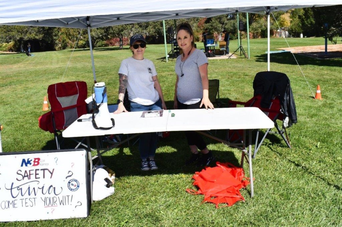 Two women stand at an outside booth at a safety fair and smile for a picture