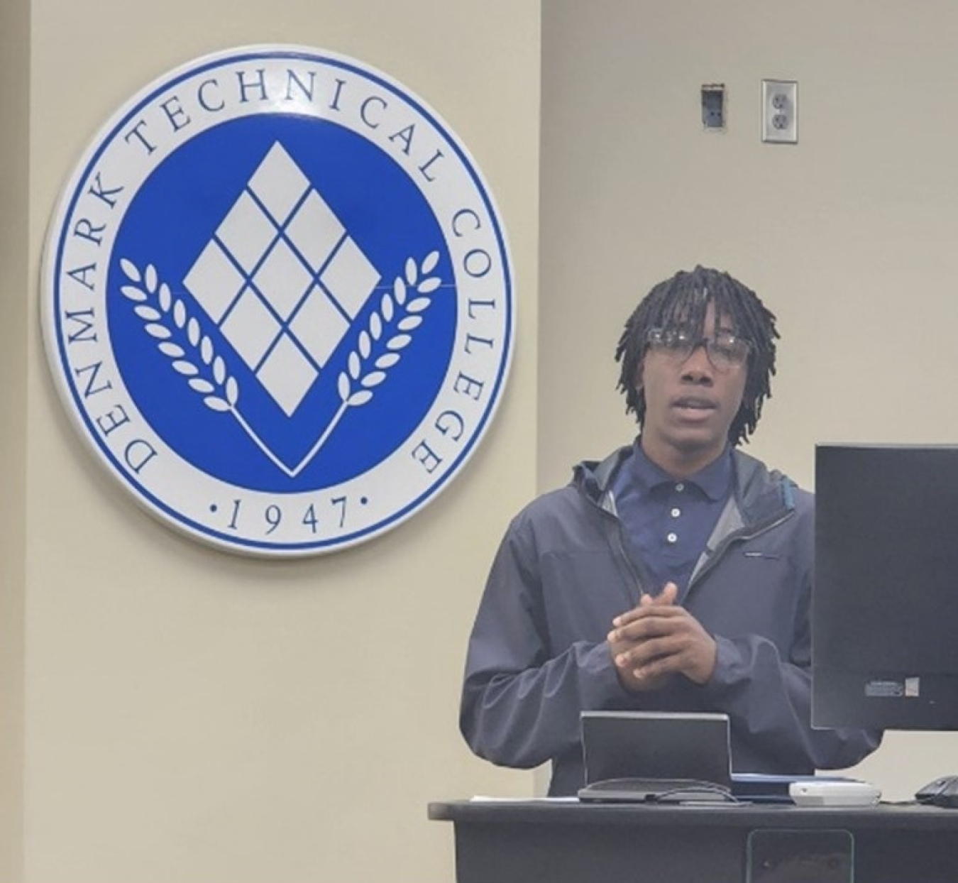 A student stands at a podium and speaks to an audience not seen behind the camera