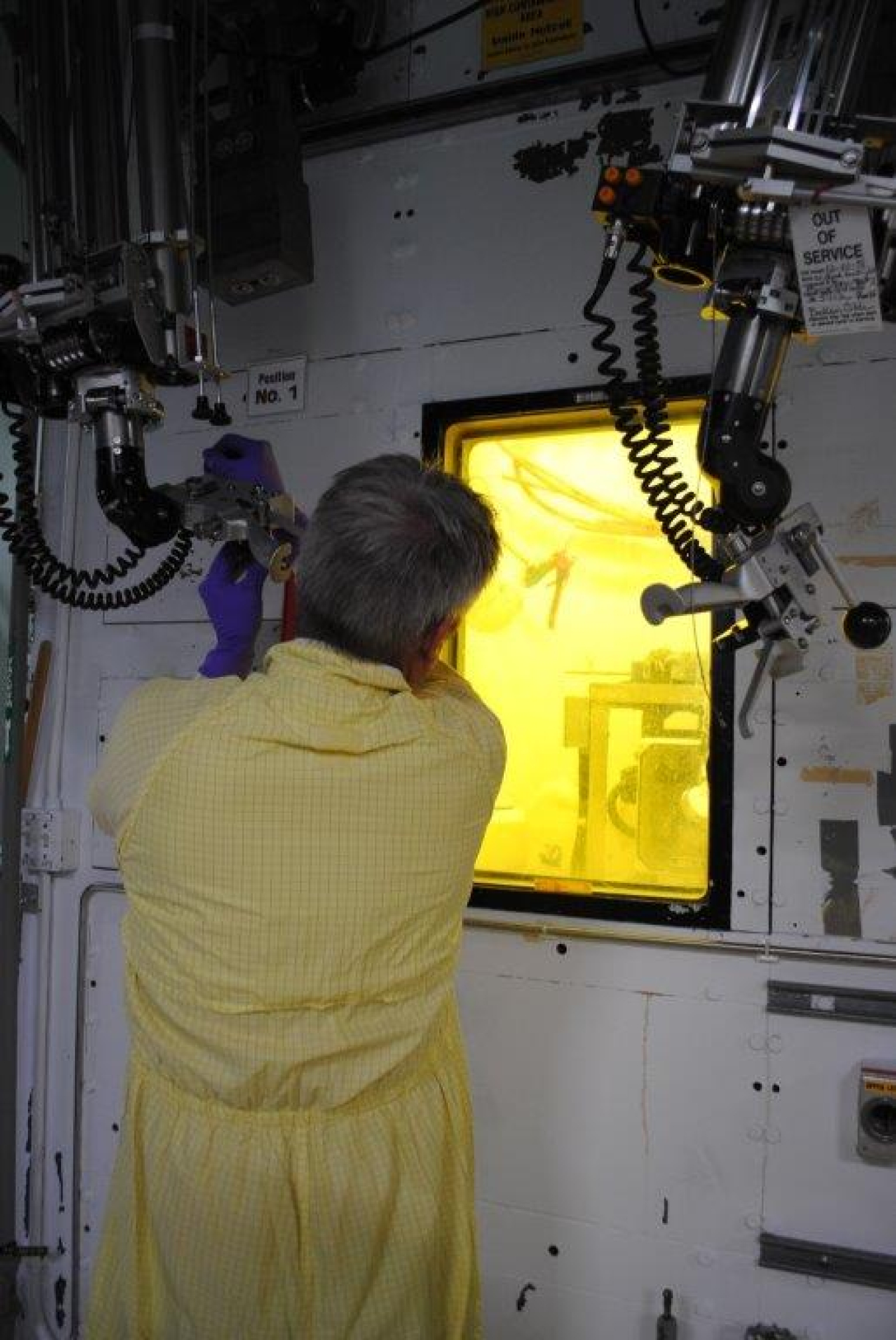 An employee in protective gear working on a hot cell machine 