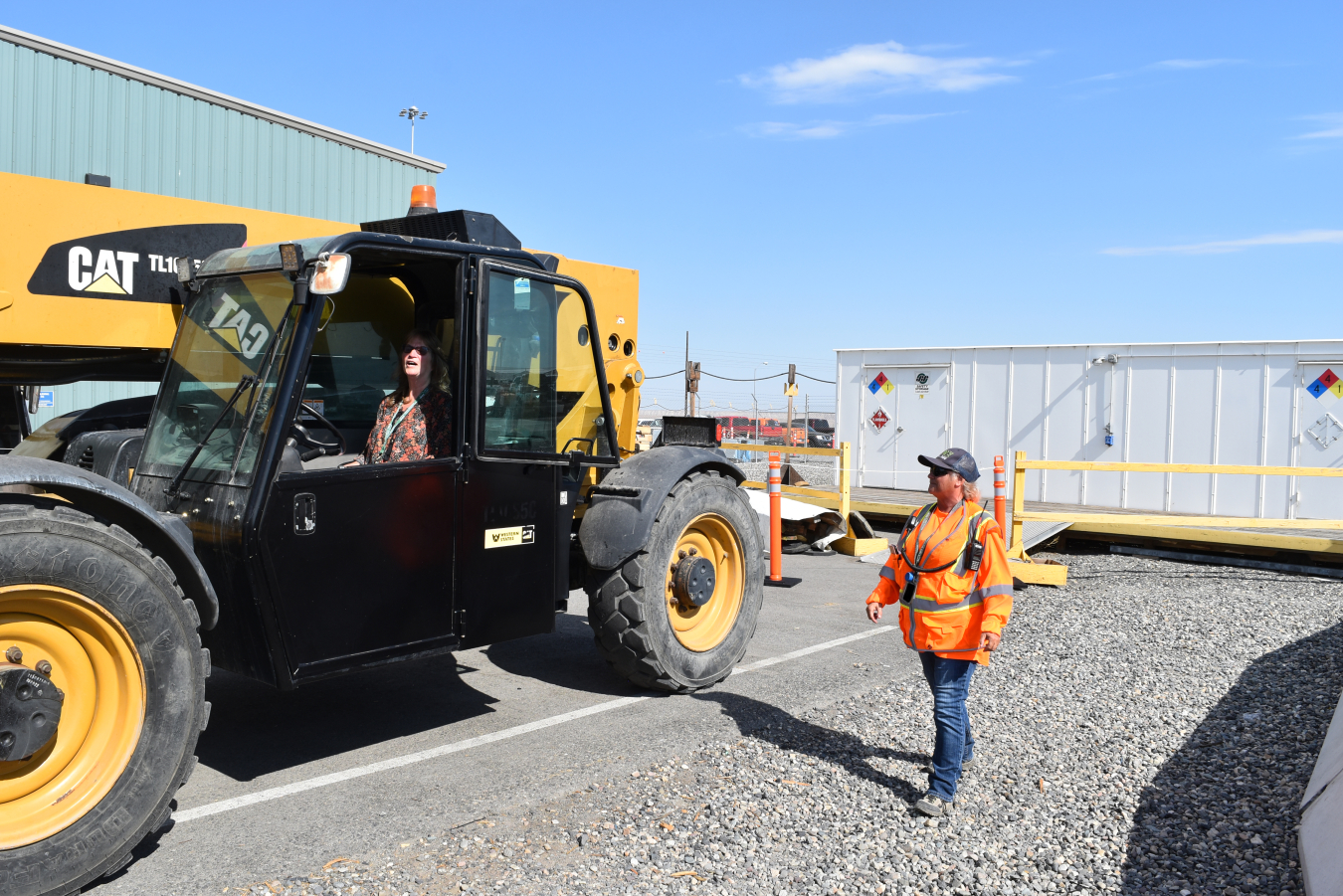 One employee walks beside a yellow construction vehicle being operated by another employee