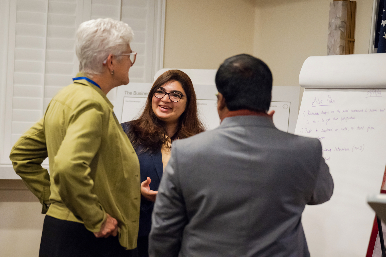 Three people converse in front of a flip chart. 