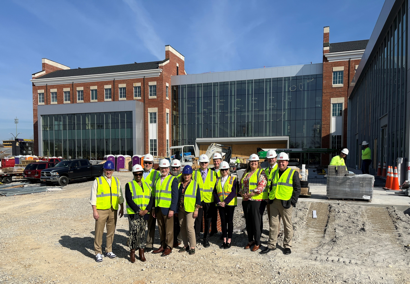 A group of people pose for a group picture in construction gear outside of a construction site