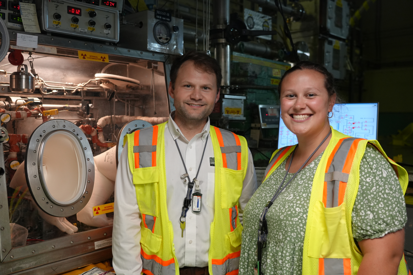 Two interns wearing neon safety vests smile beside laboratory equiptment