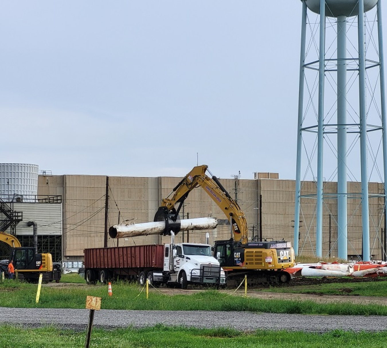 An excavator lifts a support leg over a truck.