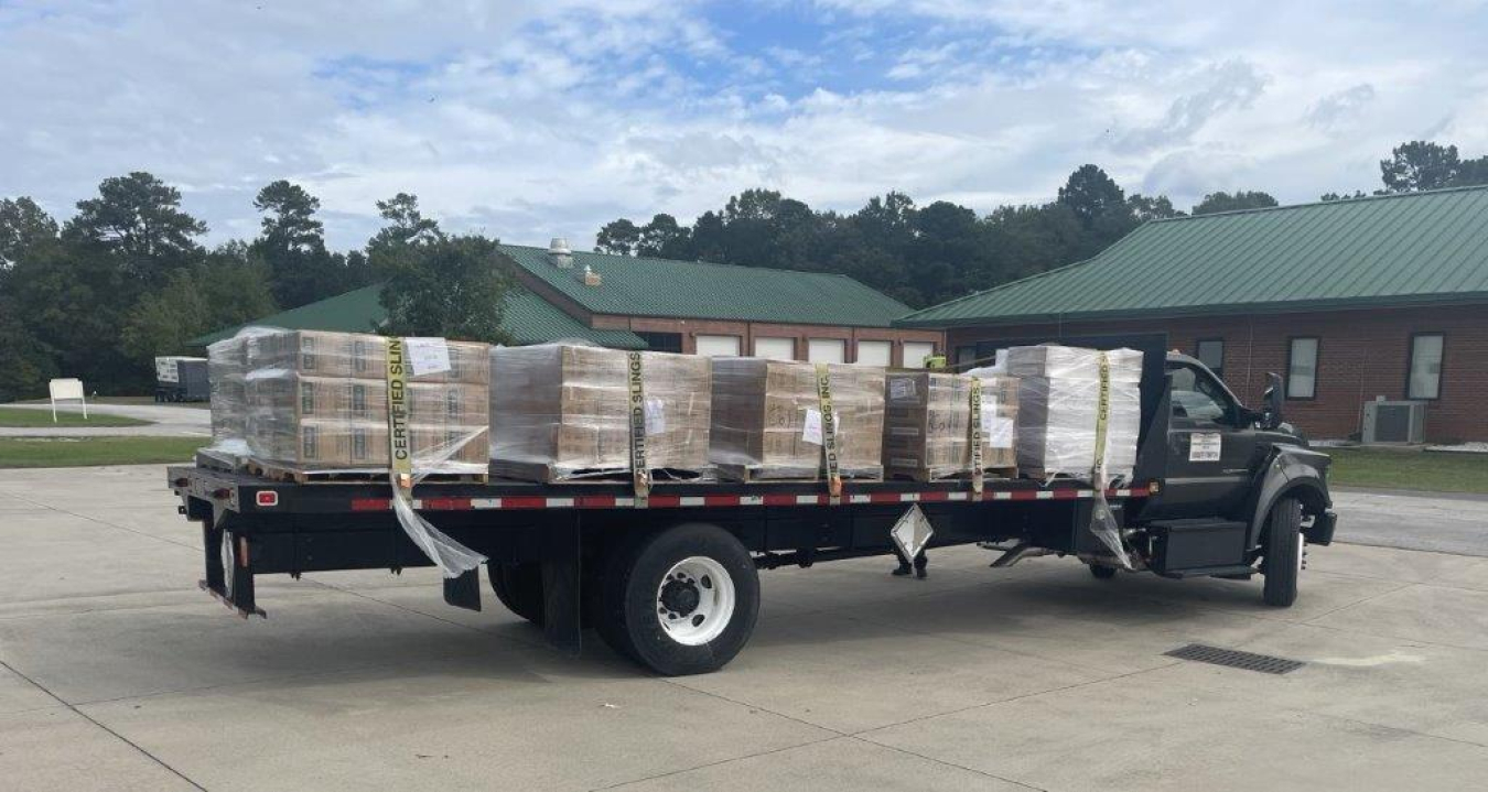 A long bed truck with lots of cardboard boxes loaded onto it and strapped down