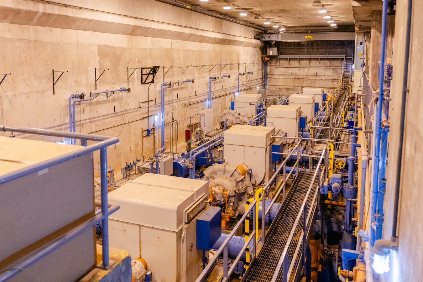 The inside of a large facility building with lots of white and blue pumps and valves inside