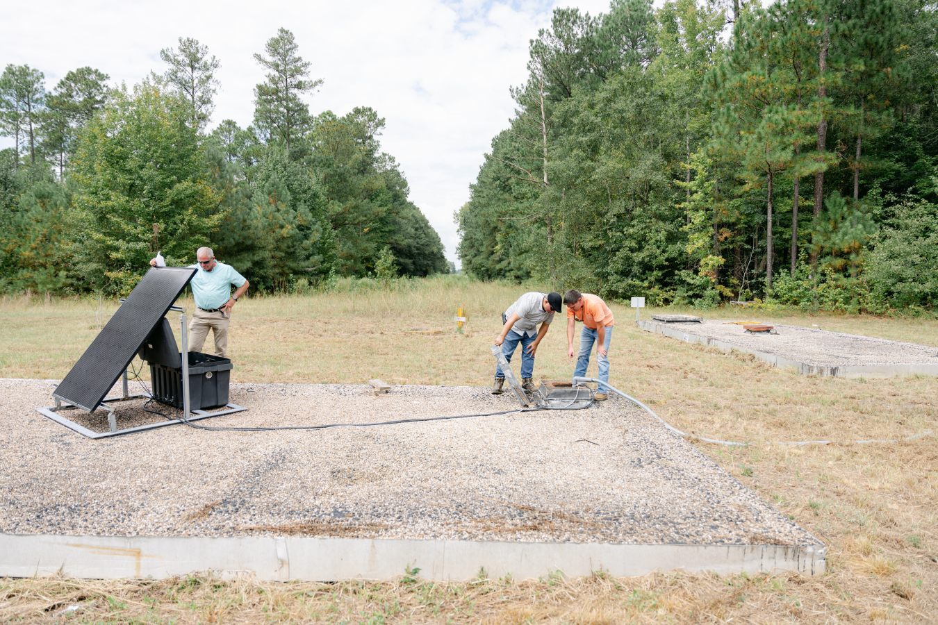 Three employees stand outside and work on a solar panel
