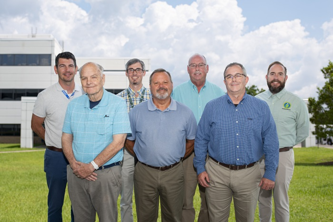 A group of men pose for a group picture outside of a white building