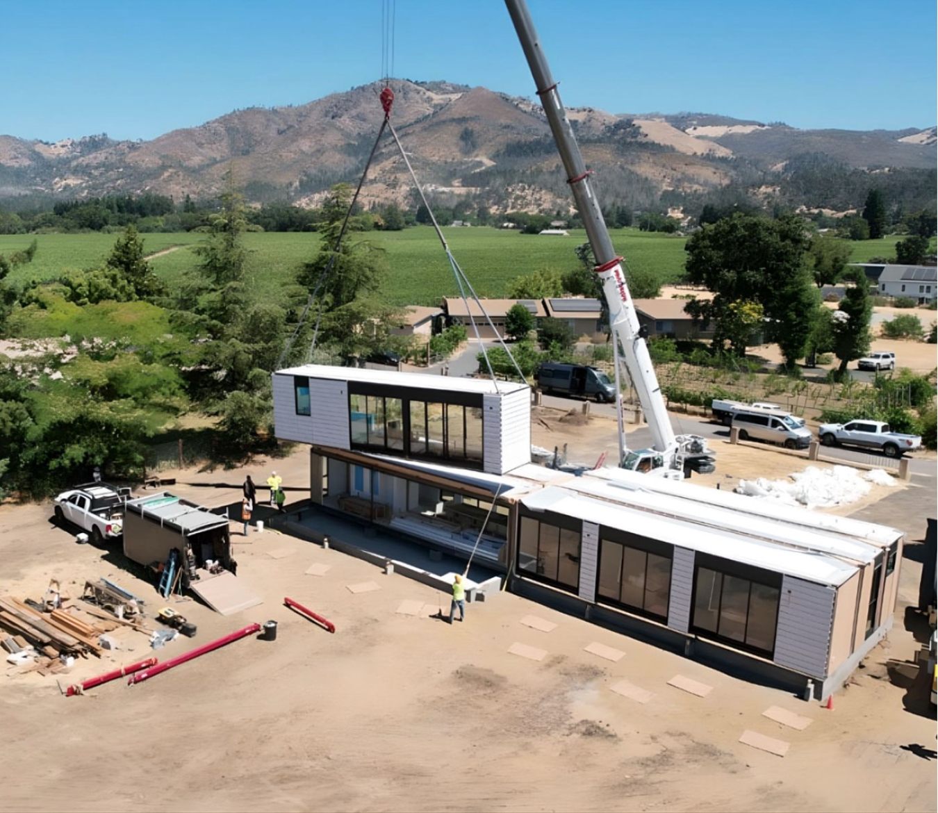 A remote work site with a crane lowering a building segment into place, with mountains in the background.