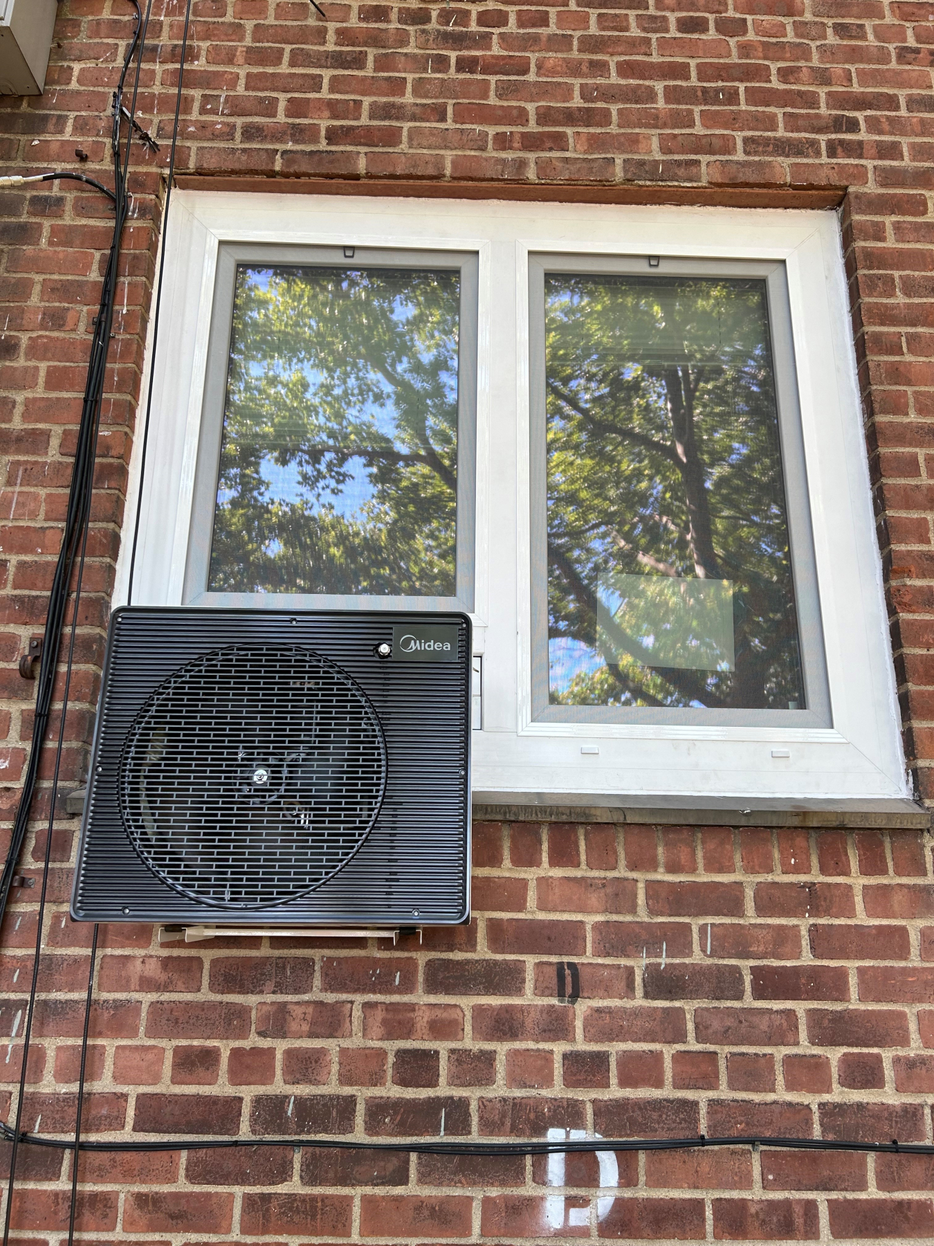 A window with a heat pump at the bottom. The outside view is on a brick wall.