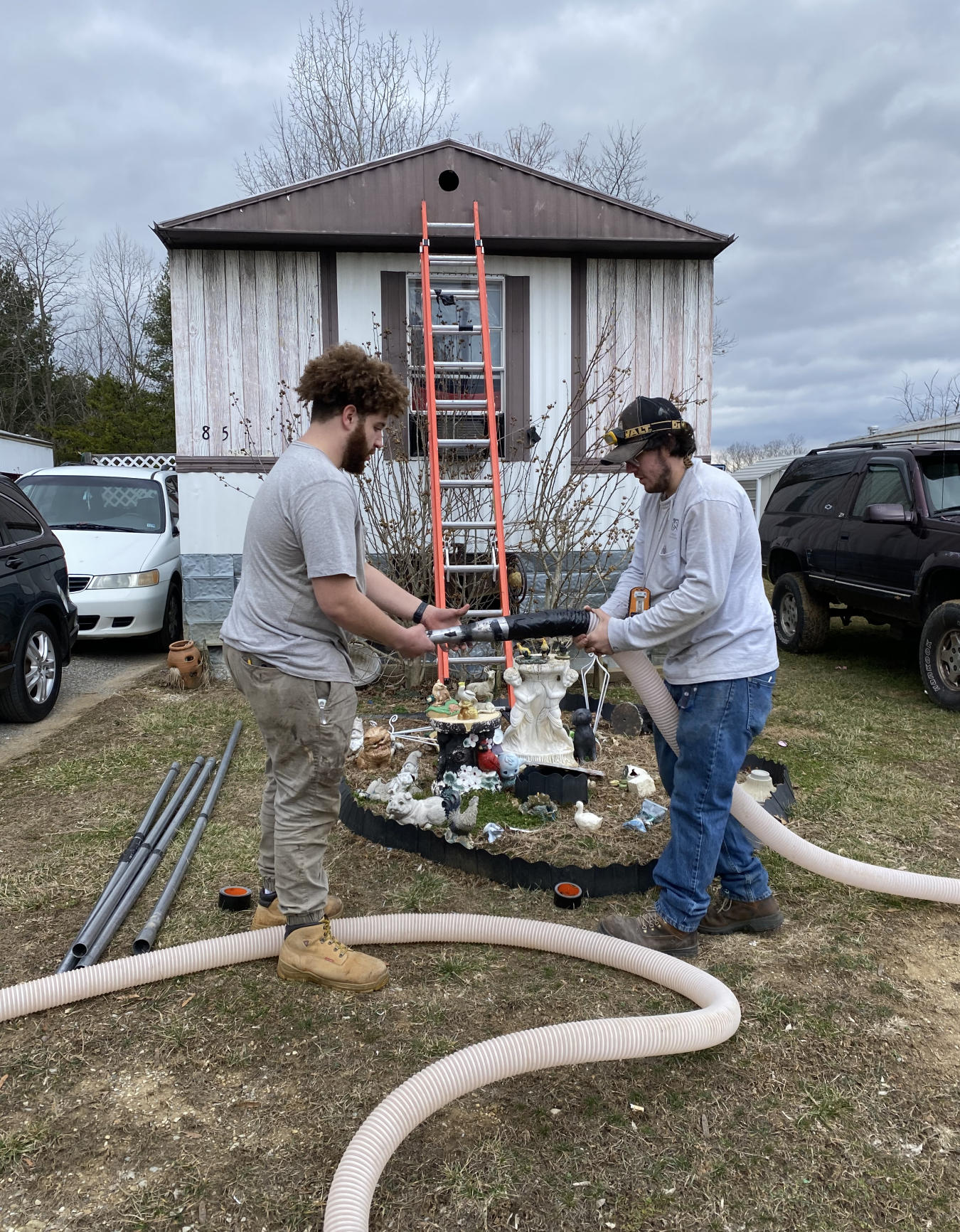 Two people hold a tube as they work in front of a mobile home.